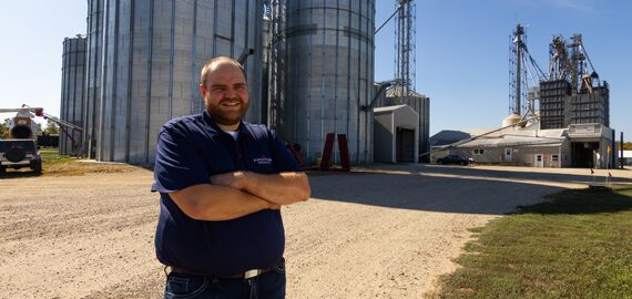 A feed mill manager stands in front of a pig feed mill.