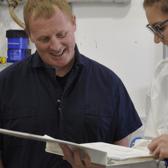 A farmer and a farmstats employee stand in a barn and look at swine data in a binder.