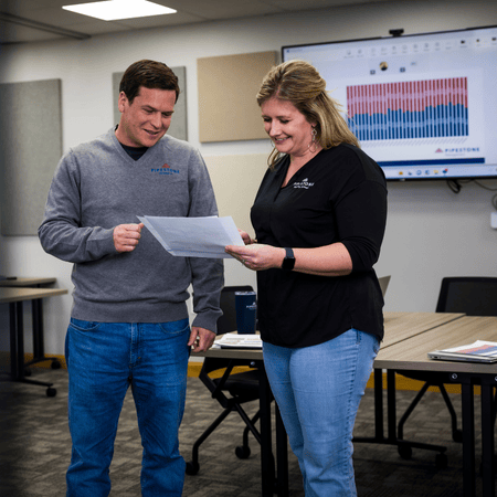Two team member stand in a meeting room looking at swine data with a graph behind them.