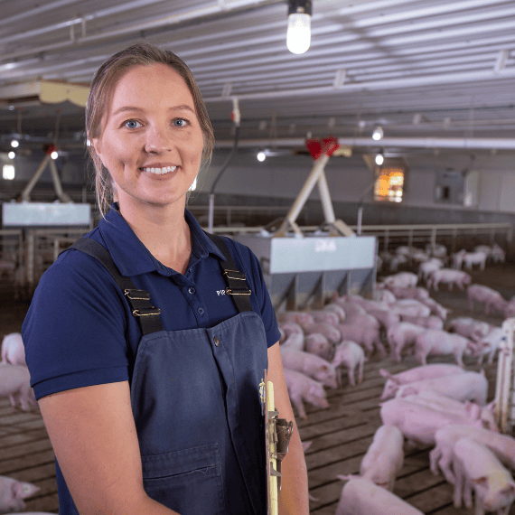 A FarmPro consultant standing in a swine barn pen with a clipboard.