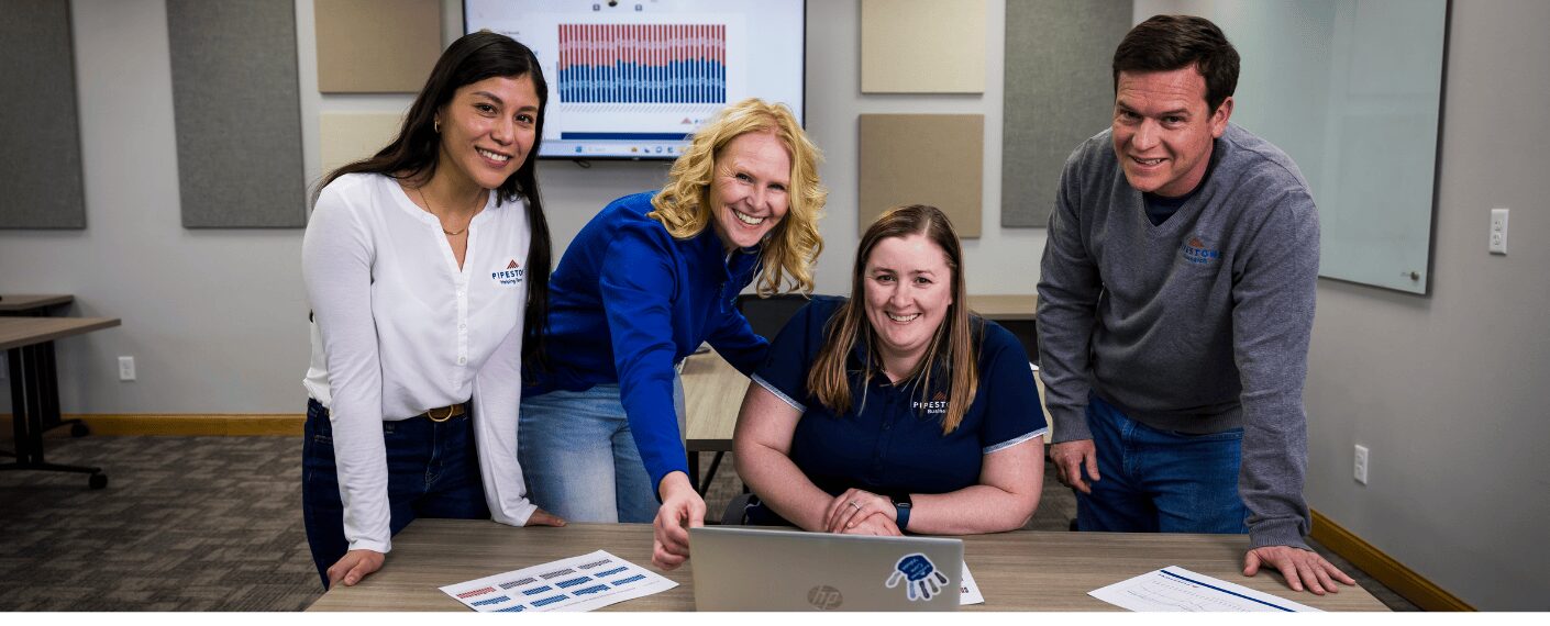 Four employees stand and sit in a meeting room with swine data and a computer in front of them.