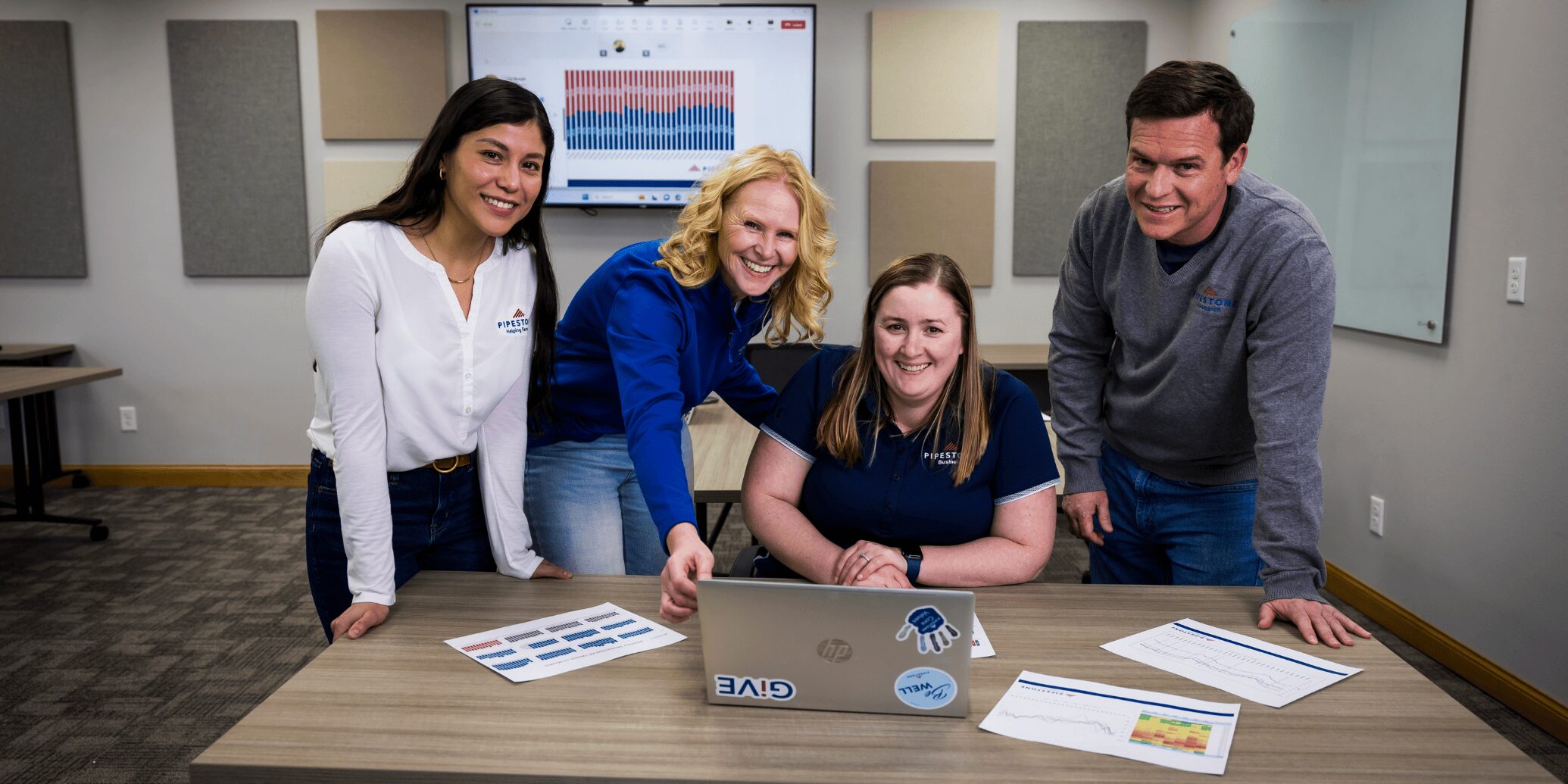 Four employees stand and sit in a meeting room with swine data and a computer in front of them.
