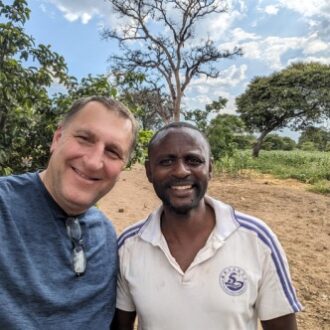 Two men smiling, trees and grass behind them.