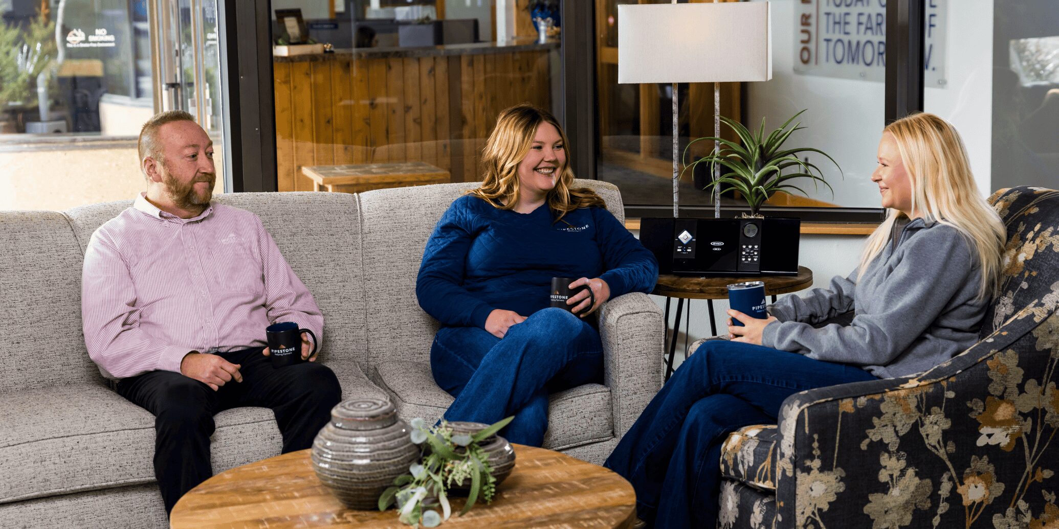 Three pipestone team members sit on a couch and chair in the office having a conversation.