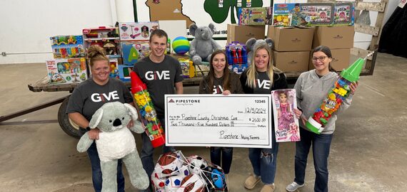 A group of pipestone volunteers hold up children's toys and a check to be donated.