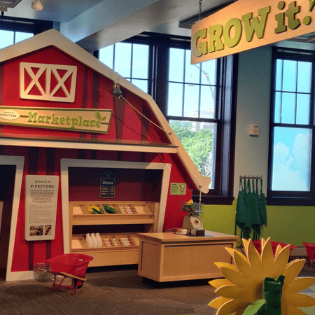 A picture of display of a red barn and marketplace at the Washington Pavilion Grow It exhibit.