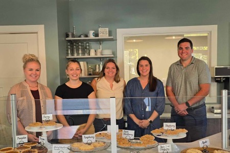 A group of pipestone volunteers stand in front of a table with pies and pastries on it.