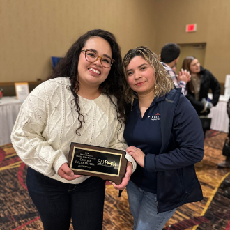 Two women pose with a swine award plaque at a banquet.