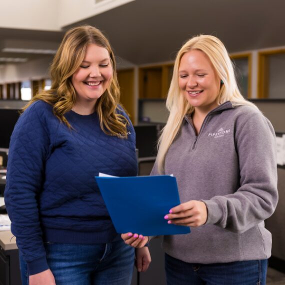 Two smiling swine nutrition specialists review a feed order inside an office.