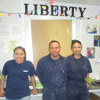 Three sow farm employees standing in front Liberty farm name on the wall.