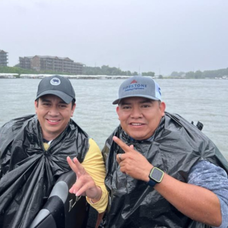 Two men sit in a boat with ponchos on.
