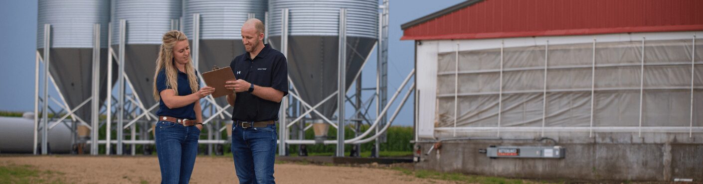 Two swine nutrition experts stand in front of feed bins and discuss pig diets.