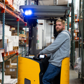 A pipestone employee driving a forklift in an animal health products warehouse.