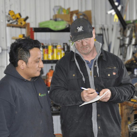 A farmer and an employee stand in a shed while going over a list of swine chores needed to be done.