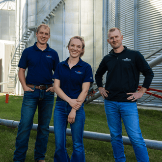Three pipestone employees standing in front of multiple grain bins and smiling.