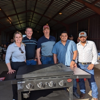 A group of pipestone workers stand behind a grill at a picnic event.