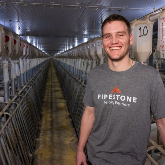 An employee stands smiling in a row of automatic feeders in a swine barn.
