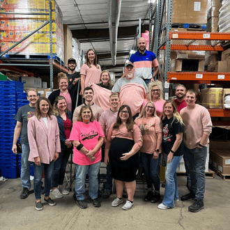 A group of employees wearing pink taking a group photo in an animal health products warehouse.