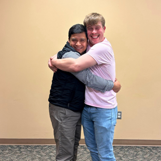 Two men smile at the camera while hugging.