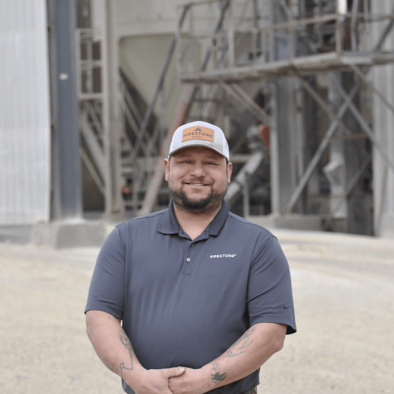 A pig feed mill manager stands outside of a mill smiling.
