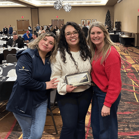Three team members pose for a photo celebrating a team member's award for pork production.