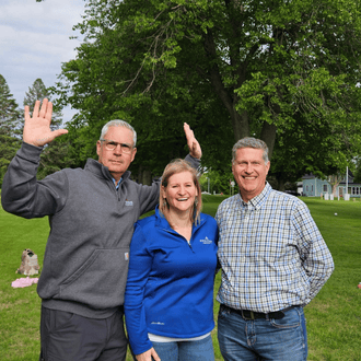 Three people stand joyfully outside at a company picnic.