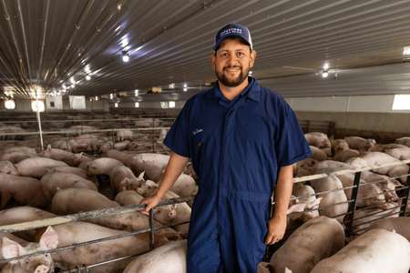 A veterinary physician assistant smiles inside of a pig farm wearing coveralls.