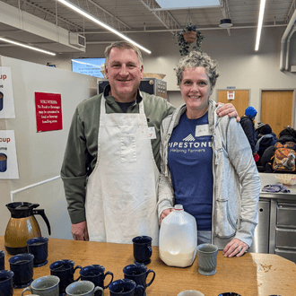Two employees volunteer at an event and pour milk for attendees.