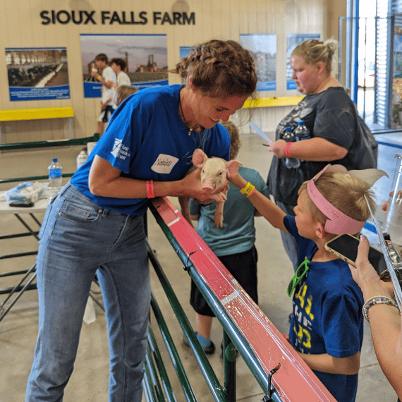 An employee volunteering at the Pipestone Discovery Barn holds a piglet for children to touch.