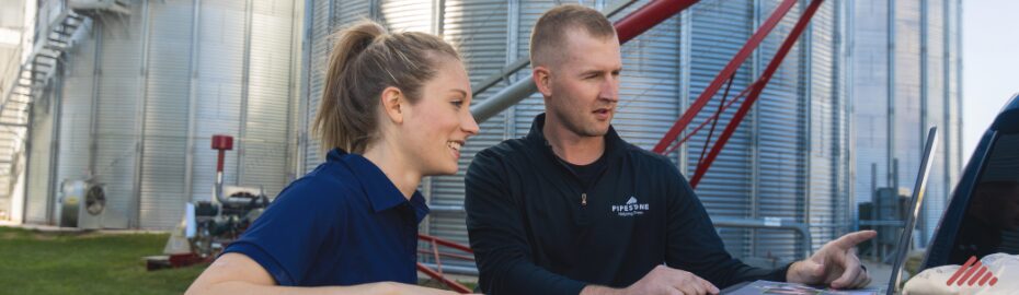 A swine nutritionist discusses swine financial information on a laptop with a Pipestone FarmBooks representative.