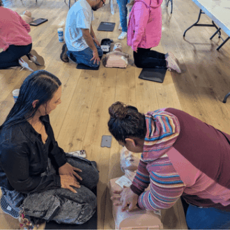 Two women practice CPR training on a dummy.