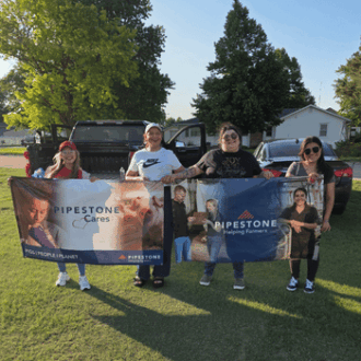 Four women hold up two Pipestone banners outside.