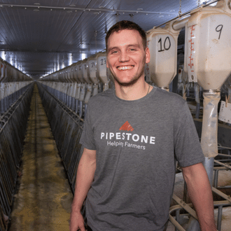 A Pipestone team member stands in front of feeding equipment inside of a sow farm.
