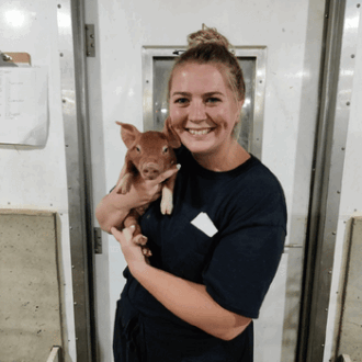 A swine veterinarian student poses with a piglet inside a sow farm..